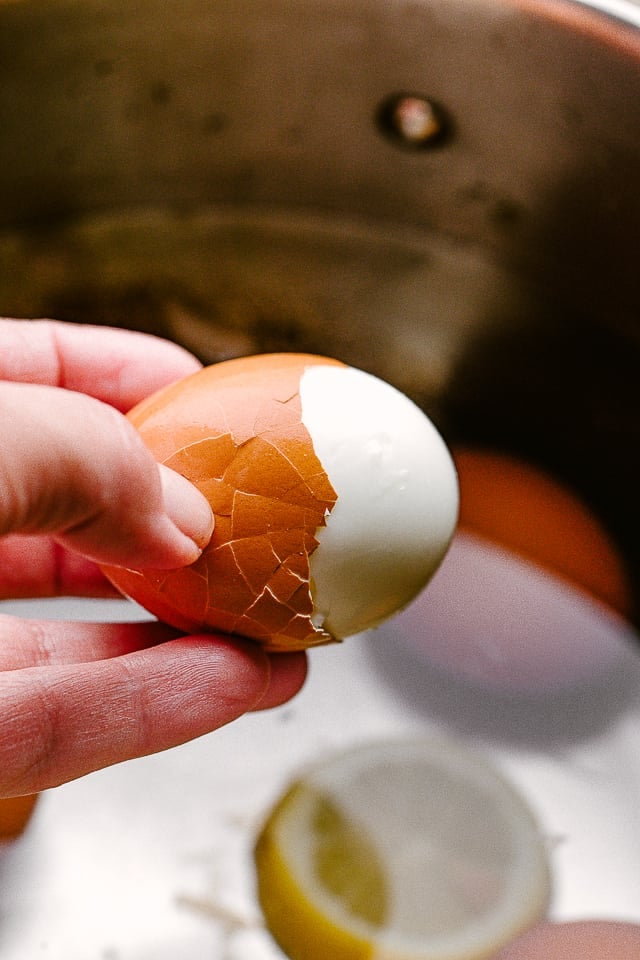 A hand holding an egg while peeling it.