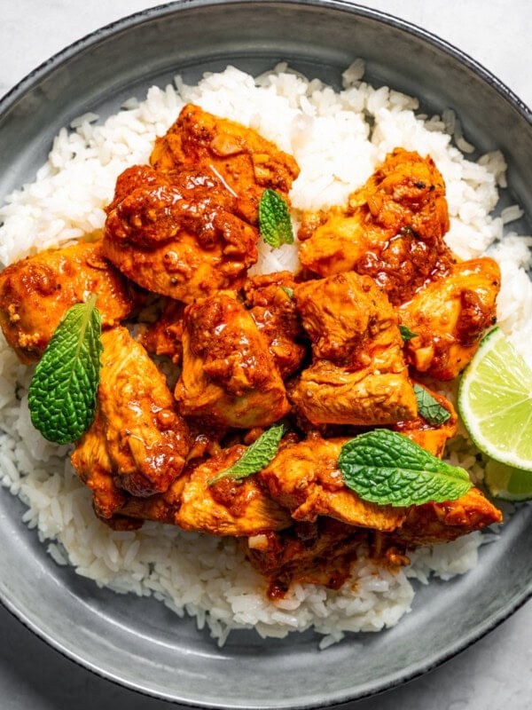 Harissa chicken served over rice and garnished with fresh green herbs and lime wedges.