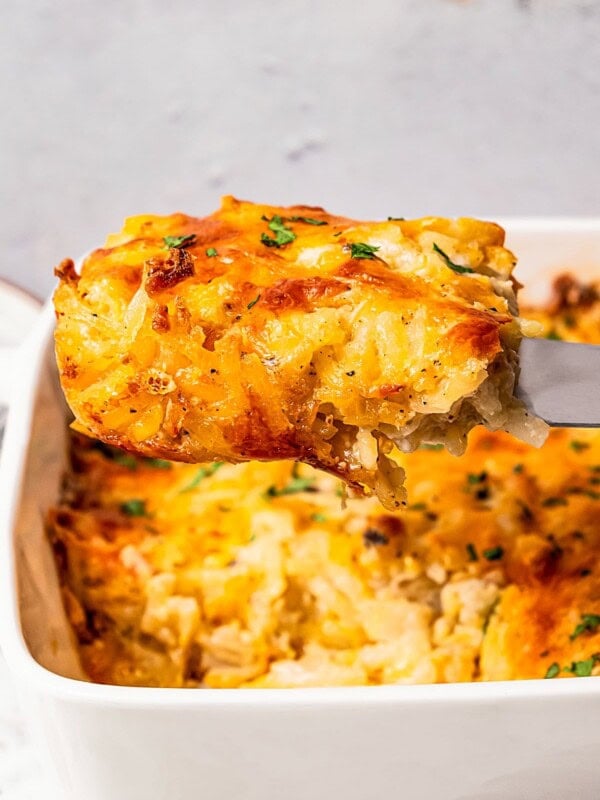 A spatula pulling out a slice of hash browns in a casserole dish.