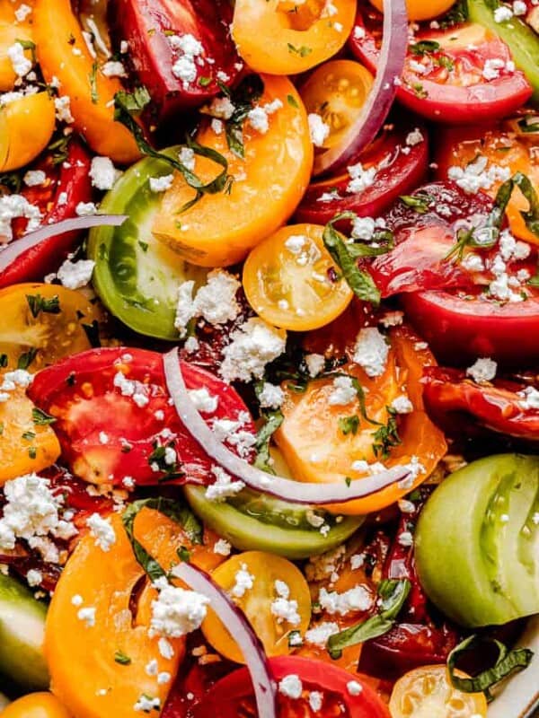 close up shot of wedges of colored tomatoes topped with slices of red onions and crumbled feta cheese