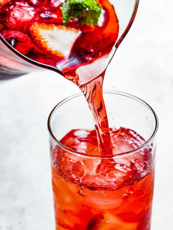 Pouring hibiscus iced tea from a pitcher into a drinking glass.