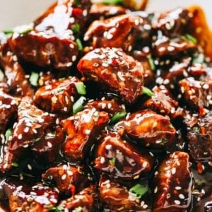 Close-up image of Honey Garlic Steak Bites garnished with sesame seeds and greens, and served in a bowl.