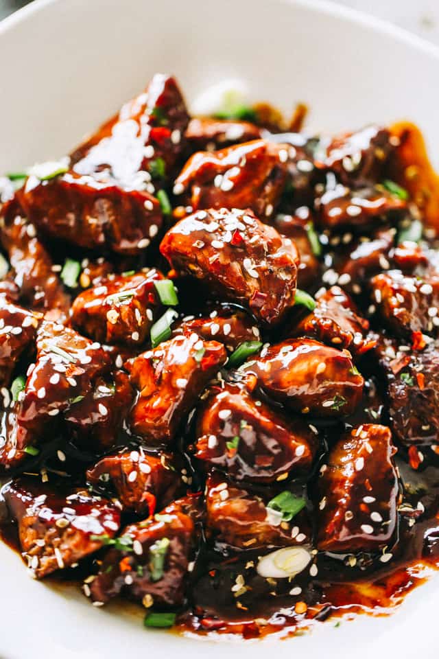 Steak Bites served in a white bowl and garnished with green onions and sesame seeds.