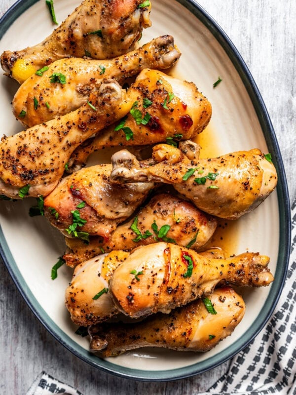 Overhead view of honey soy chicken drumsticks arranged on a white oval platter with a blue rim.