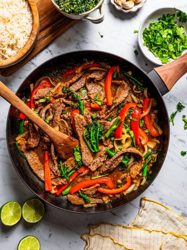 Stirring through steak slices, broccoli florets, and sliced red bell peppers in a skillet.