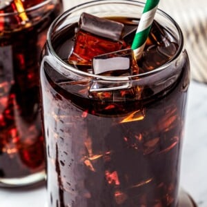 Close-up of Iced Americano served on a wooden coaster with another glass of coffee placed behind it.