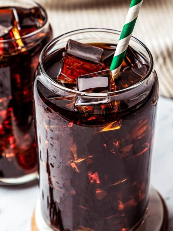 Close-up of Iced Americano served on a wooden coaster with another glass of coffee placed behind it.