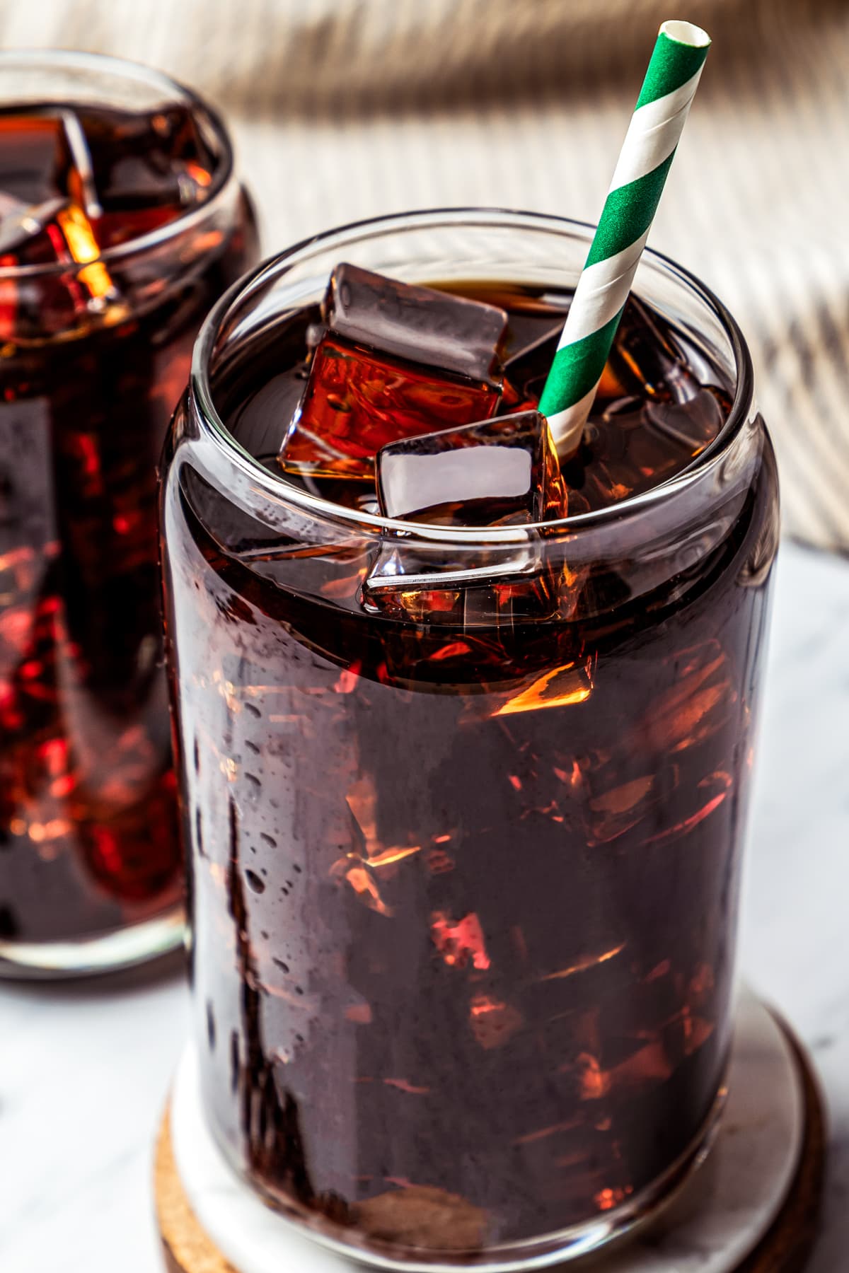 Close-up of Iced Americano served on a wooden coaster with another glass of coffee placed behind it.