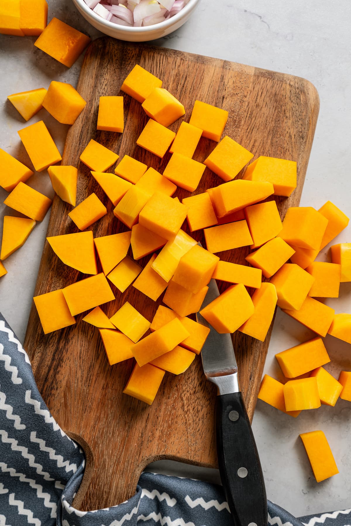 Cubing butternut squash on a cutting board.