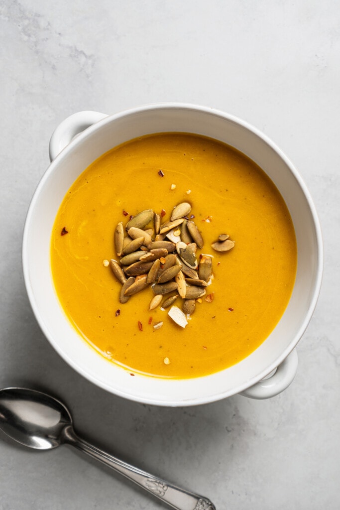 Butternut squash soup in a bowl with a spoon sitting next to it.