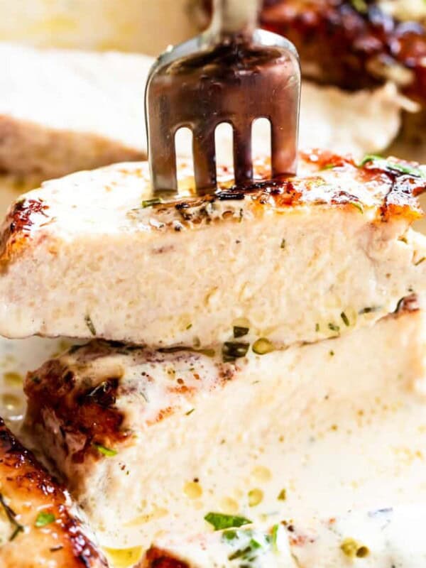 Close-up image of a fork stuck through a bite of a cream-covered pork chop.