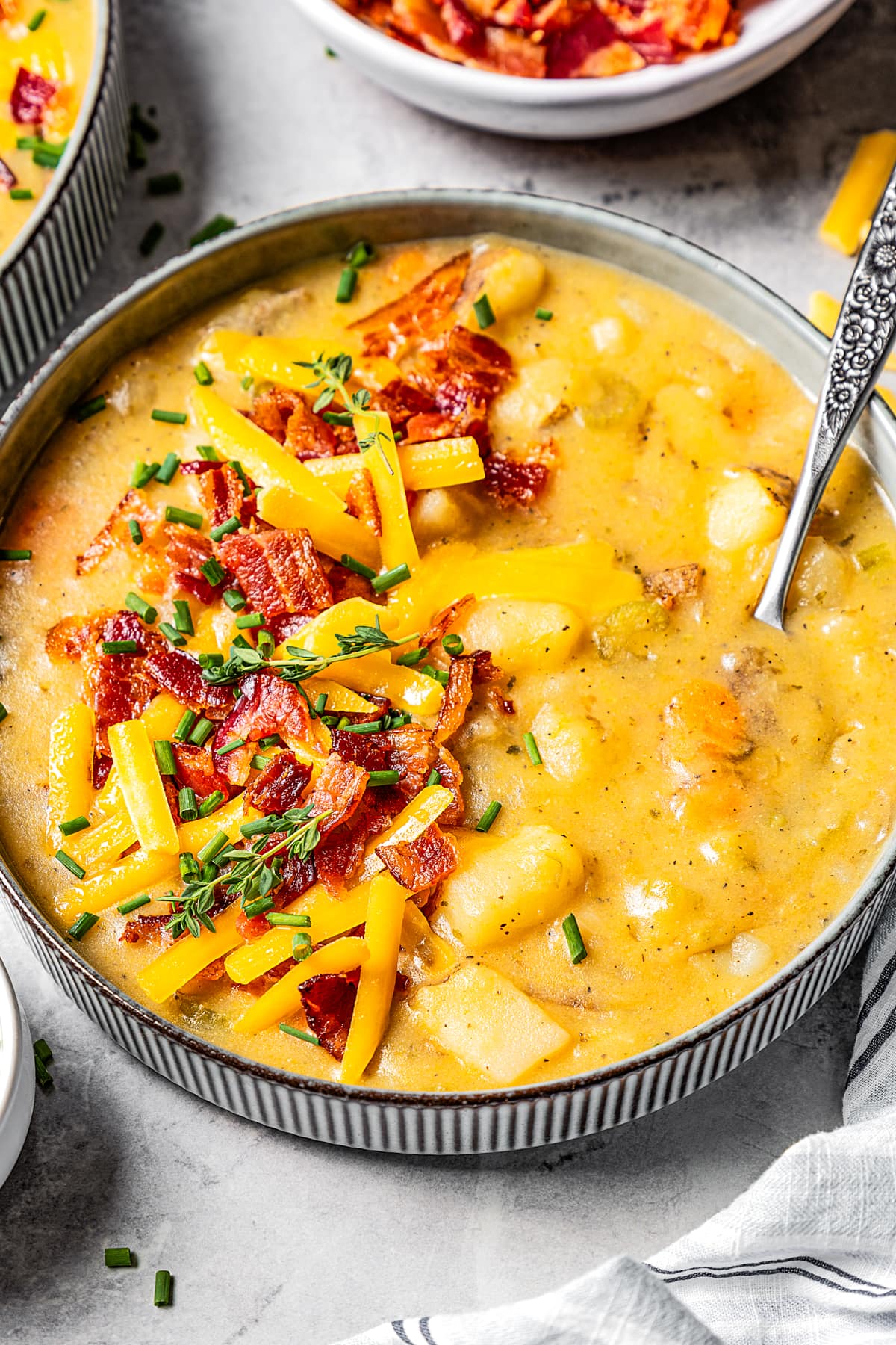 A bowl of Instant Pot potato soup garnished with chopped bacon and shredded cheddar cheese and a spoon is set inside the bowl.