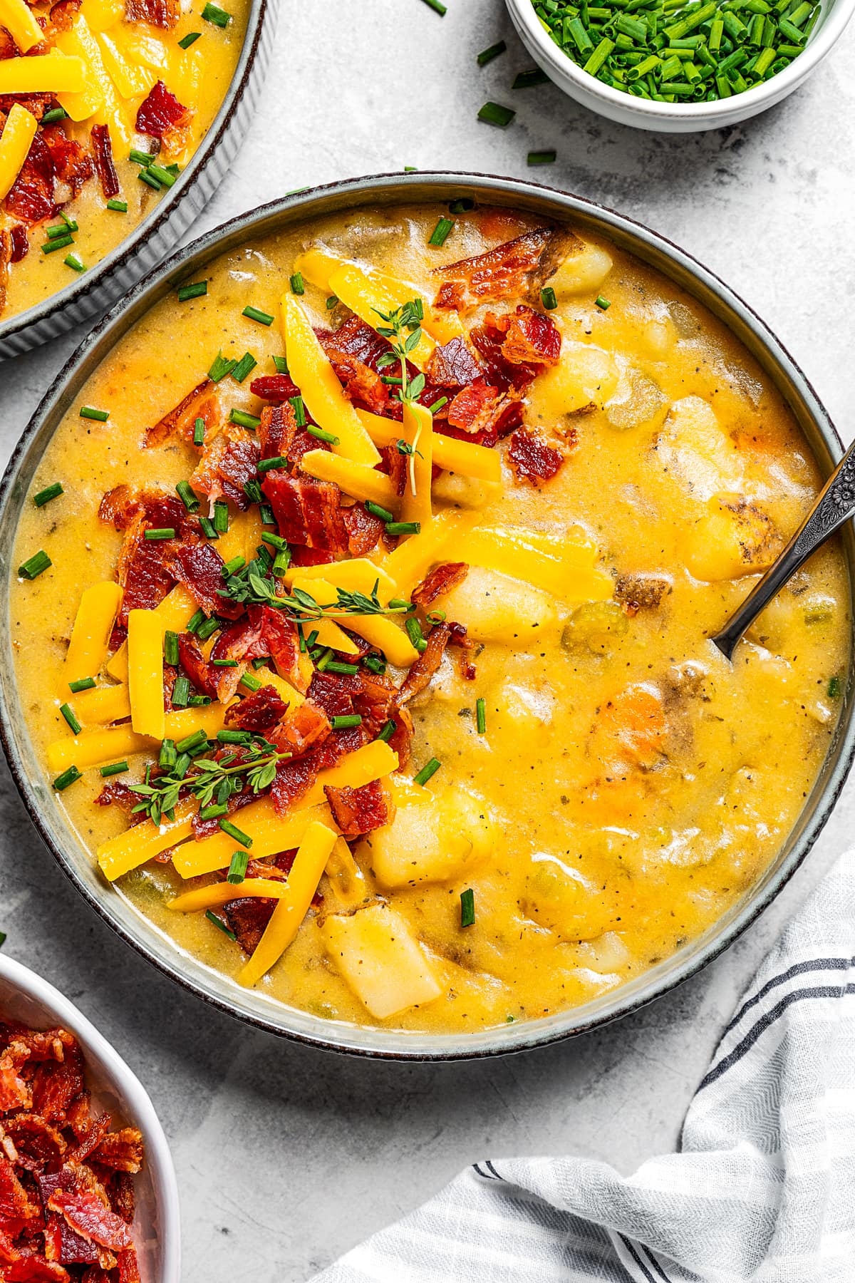 Close up overhead image of a potato soup in a bowl garnished with chopped bacon, shredded cheese, and chopped chives.