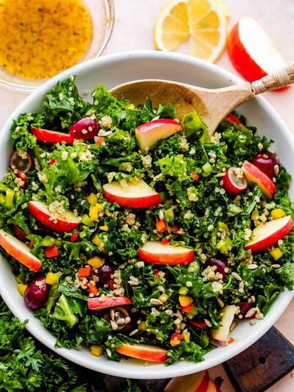 Crunchy Kale Quinoa Salad in a white bowl with a wooden spoon inside the bowl.