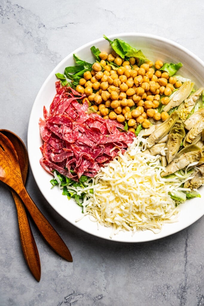 Ingredients for a La Scala chopped salad assembled in a large serving bowl next to wooden salad spoons.