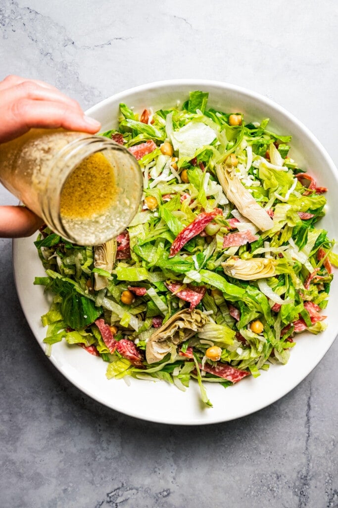 Pouring dressing over La Scala chopped salad in a large serving bowl.