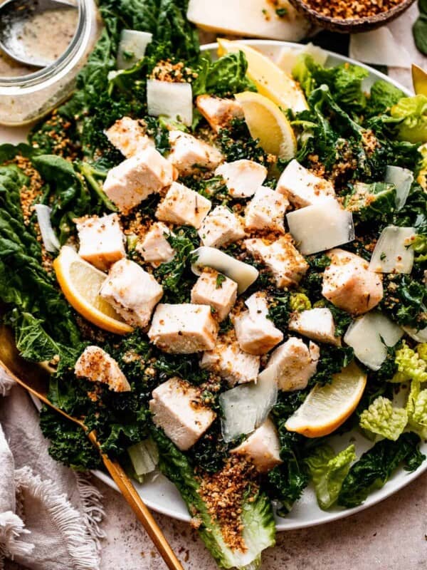 overhead shot of Lemon Kale Caesar Salad served on a plate and topped with lemons, parmesan cheese, and a sprinkle of bread crumbs.