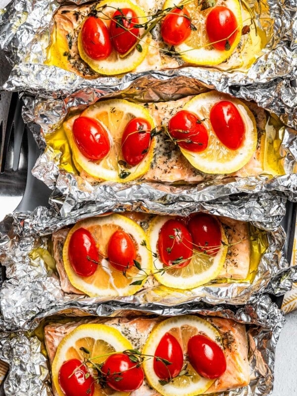 Overhead, close-up view of baked lemon pepper salmon fillets topped with lemon slices, tomatoes, and thyme inside unwrapped foil packets.