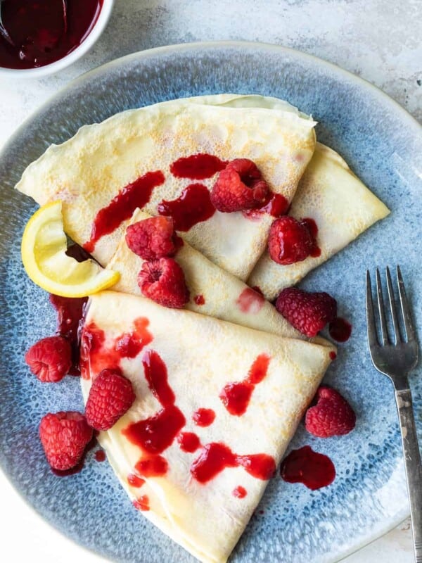 Crepes with raspberries and a lemon wedge.