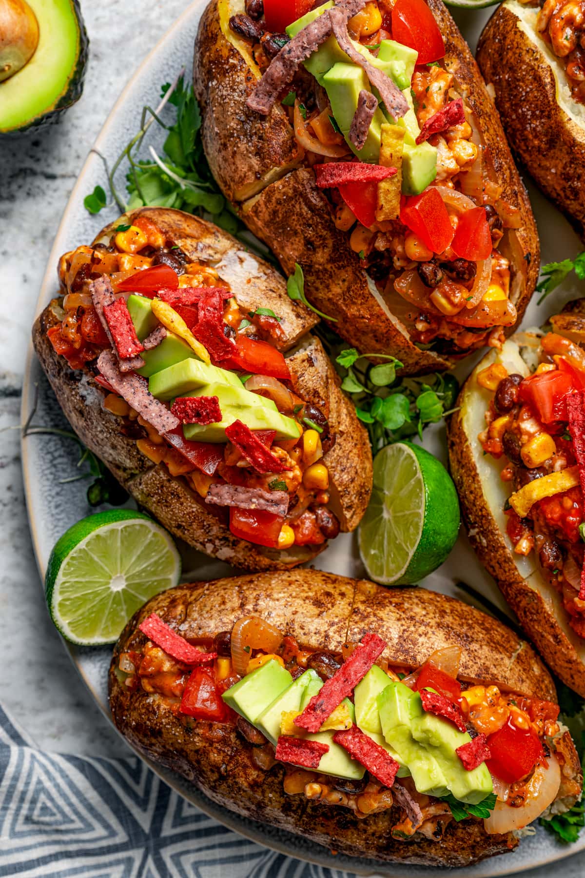 Prepared loaded baked potatoes served on a plate and garnished with lime wedges.