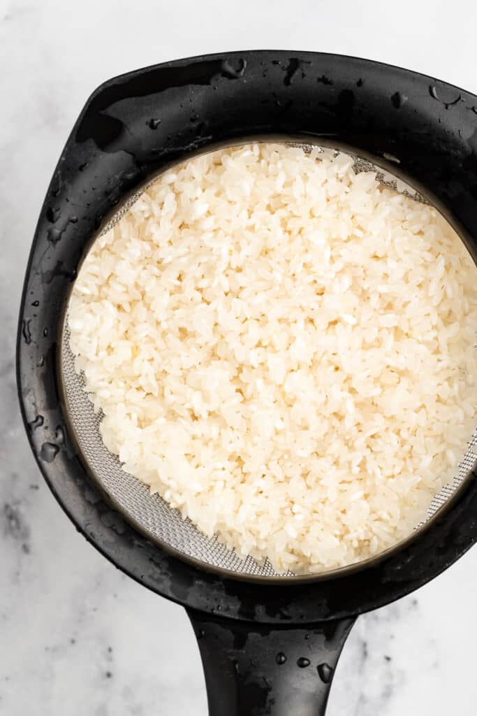 Rinsing sushi rice in a fine mesh colander.