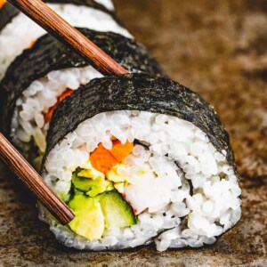 Chopsticks reaching for a slice of maki roll.