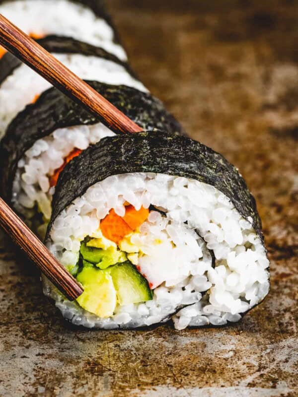 Chopsticks reaching for a slice of maki roll.