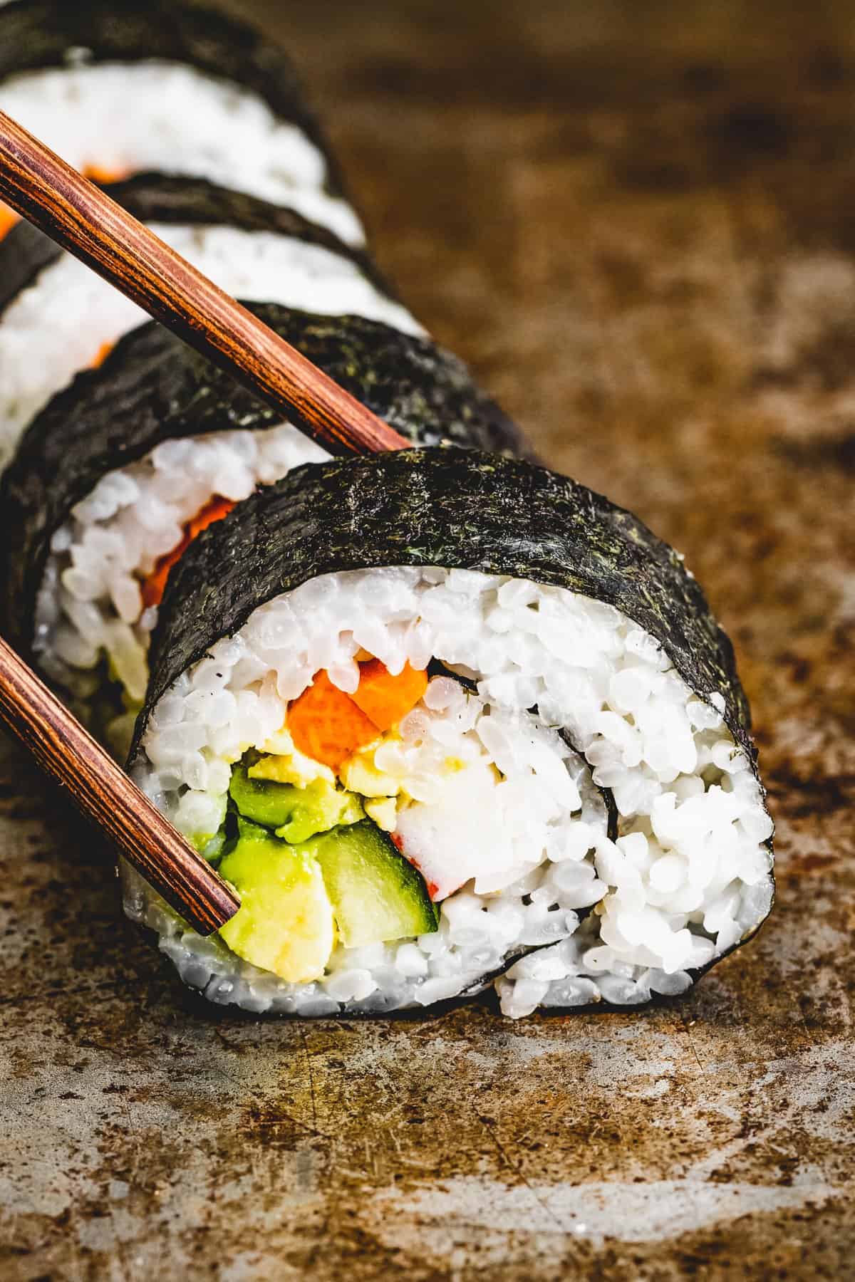 Chopsticks reaching for a slice of maki roll.