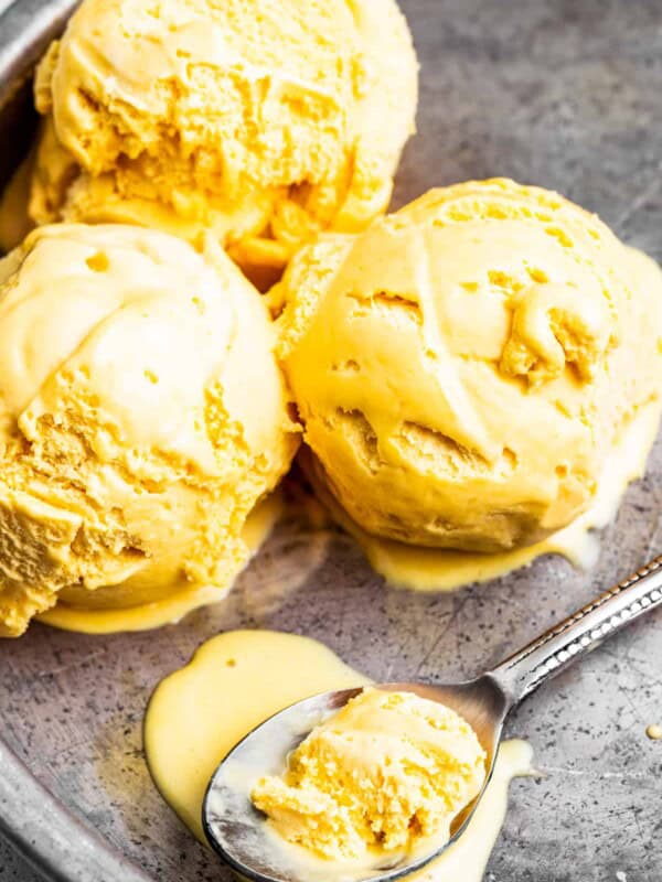 Three scoops of mango ice cream in a pan with a spoon that has mango ice cream in it.