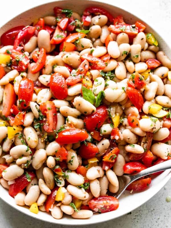 overhead shot of a salad bowl with cannellini beans, tomatoes, bell peppers, and a spoon set inside the right bottom side of the bowl.