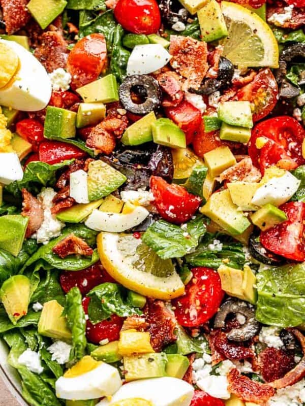 close up top view shot of boiled egg wedges, lemon slices, chopped avocados, tomatoes, and bacon set over leafy lettuce