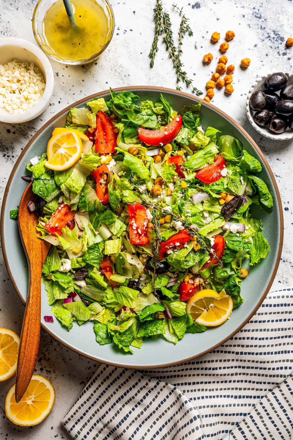 Overhead image of a salad served in a bowl with romaine lettuce, tomatoes, corn kernels, garbanzo beans, and lemon slices.