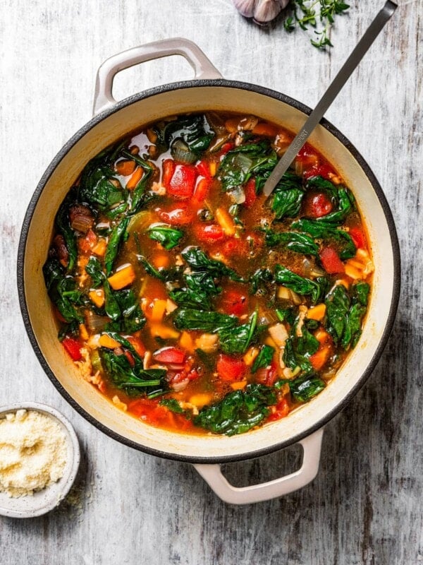 Finished minestrone soup in a large pot with a ladle, surrounded by soup ingredients.