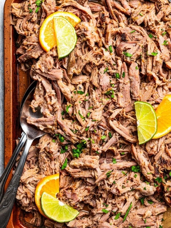 Mojo pork on a sheet pan with serving utensils set on top of the meat.