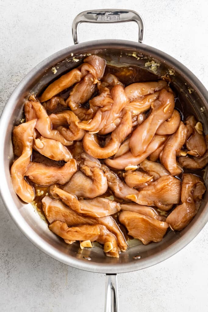 Adding marinated chicken strips to a pan.