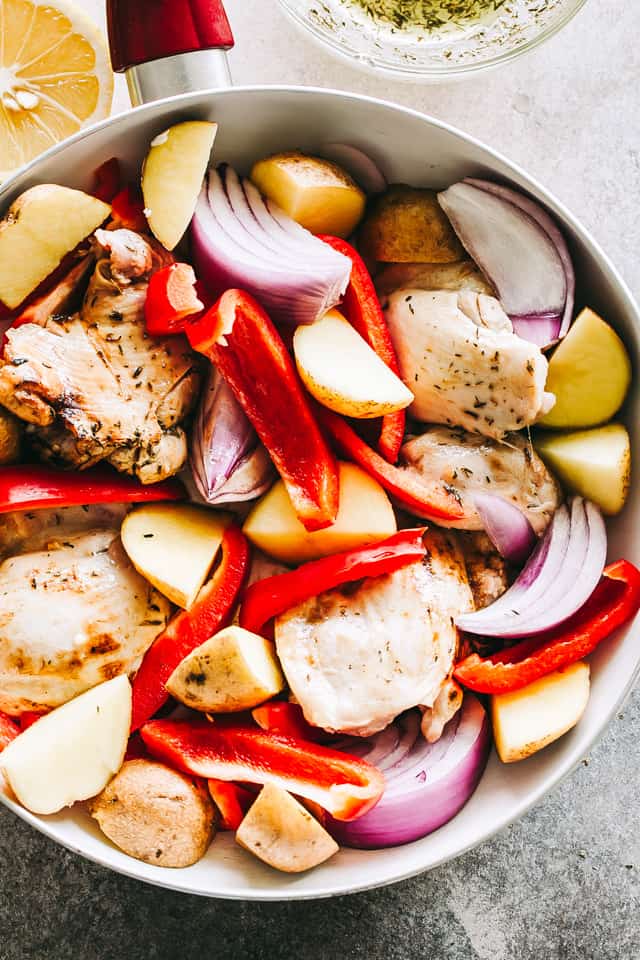 Raw chicken thighs and veggies in a skillet.