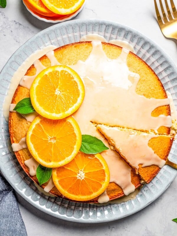 Overhead view of a glazed olive oil cake garnished with orange slices and mint leaves.