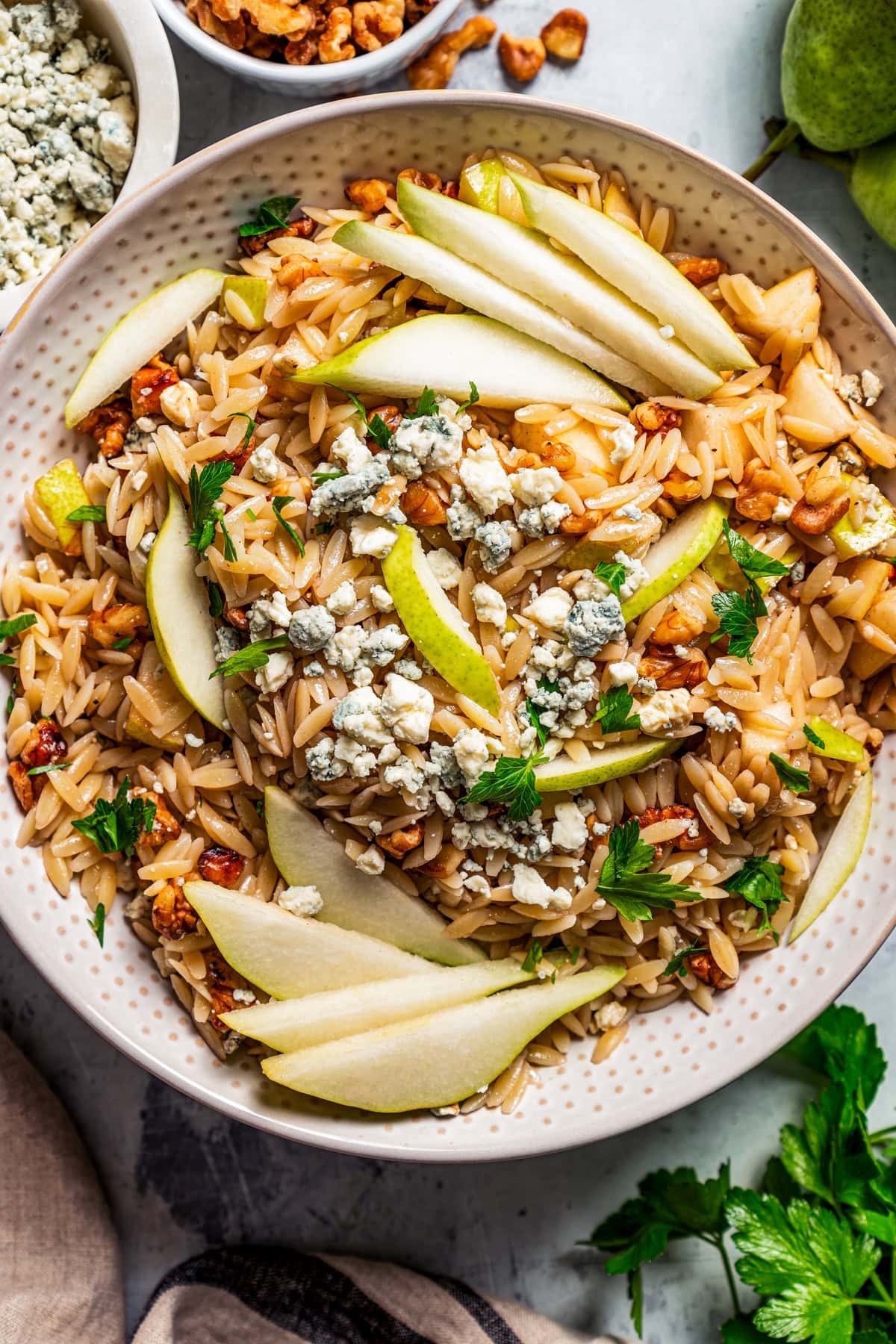 Overhead view of orzo salad with pears, walnuts and gorgonzola cheese in a bowl garnished with pear slices.