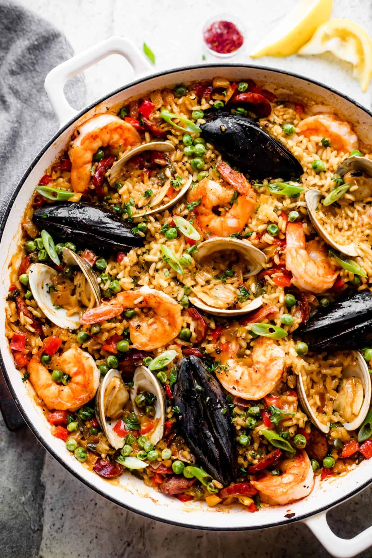 Seafood paella in a pan with rice topped with clams, shells, mussels, shrimp, sliced sausages, and peas.