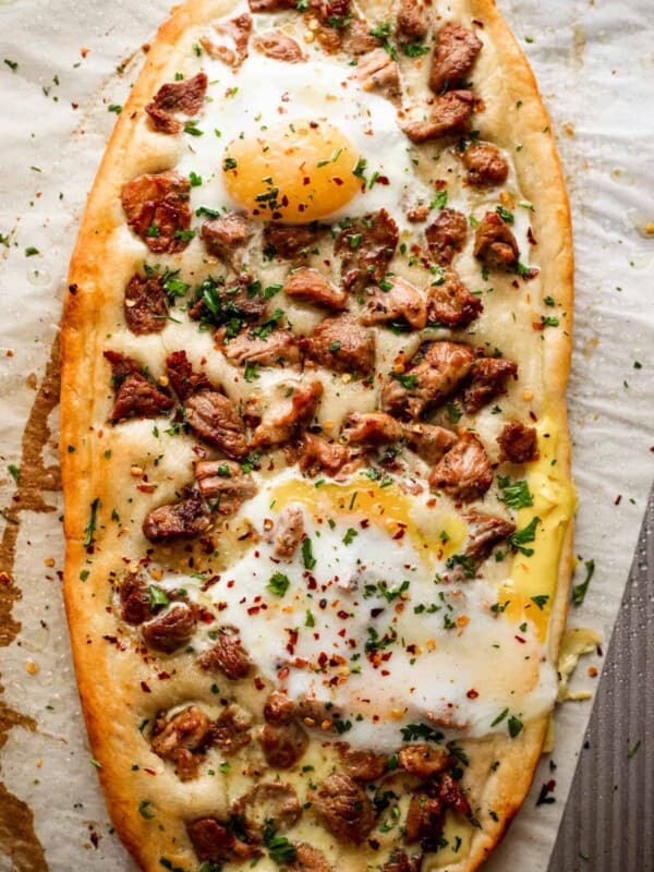 overhead shot of Pastrmajlija pizza topped with chunks of pork and fried eggs.