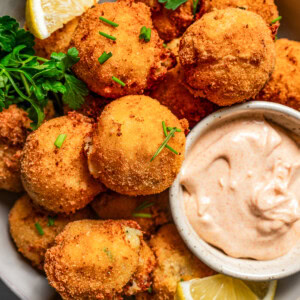 Close-up photo of potato croquettes served in a bowl with a side of aioli and lemon wedges.