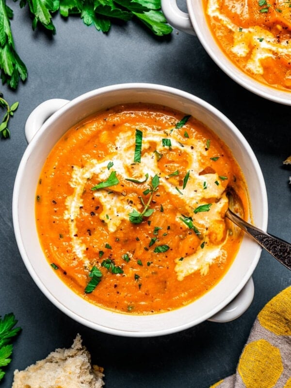 Overhead view of a bowl of pumpkin soup topped with a drizzle of cream and fresh herbs, next to a second bowl.