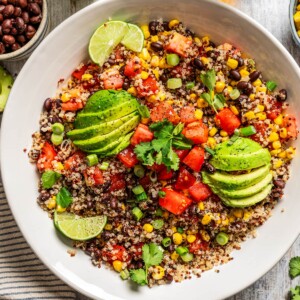 Overhead image of Quinoa Southwestern Salad in a salad bowl topped with sliced avocados and slices of lime.