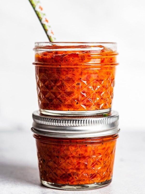 Two small jars of Ajvar stacked, with a spoon sticking out of the top jar.