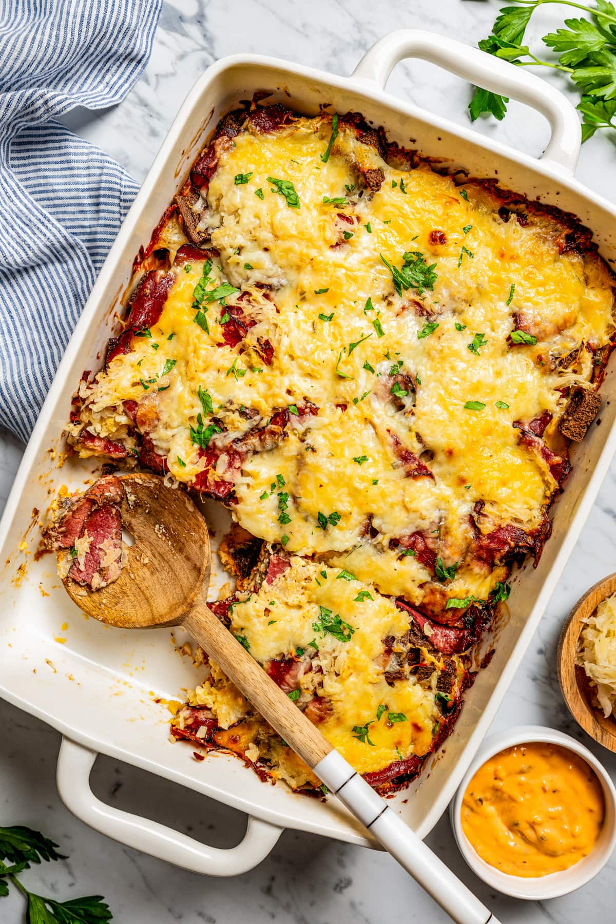 Overhead image of a Reuben casserole in a baking dish, with a wooden spoon resting inside the dish.