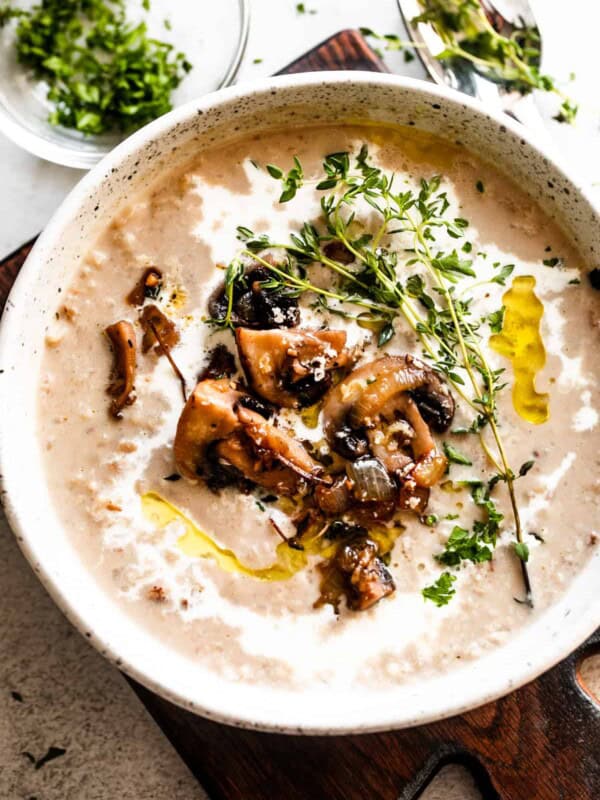 overhead photo of creamy mushroom soup and rice in a bowl garnished with whole mushrooms, greens, and a swirl of heavy cream.