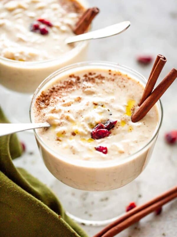 Creamy Rice Pudding Dessert in a glass cup, garnished with two cinnamon sticks and dried cranberries.