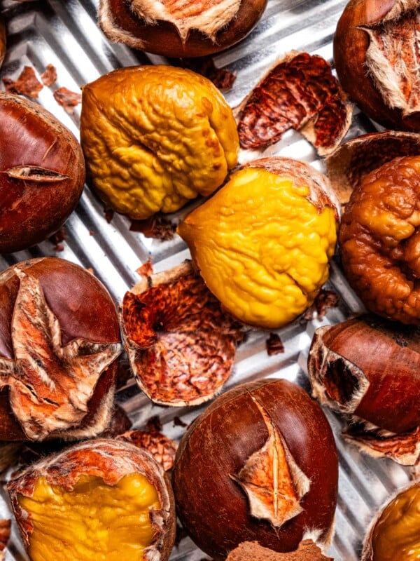 Close-up photo of roasted chestnuts, some outside of the shell and some are inside of their shells.