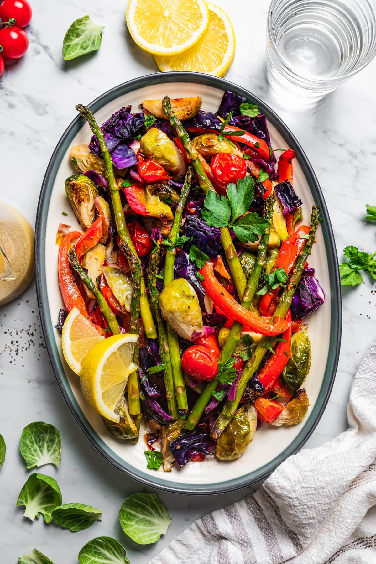 Serving platter of roasted vegetable salad with lemon wedges.