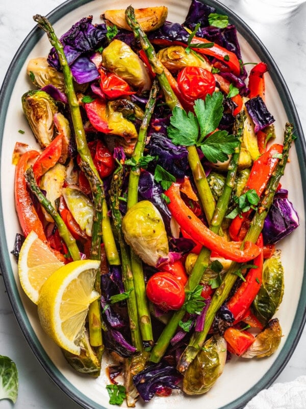 Roasted asparagus, bell peppers, tomatoes, cabbage, and brussel sprouts served on a platter with lemon wedges.